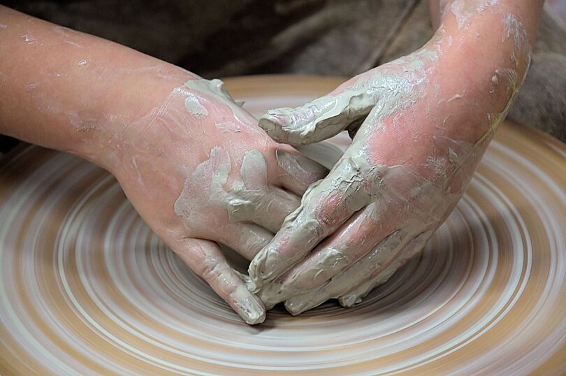 Zwei Hände arbeiten auf einer Töpferscheibe mit weißem Ton. 