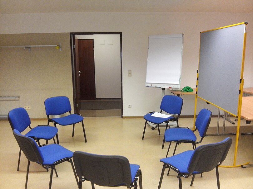 Ein Sesselkreis mit 7 blauen Sesseln steht in einem Teil eines Klassenzimmers.