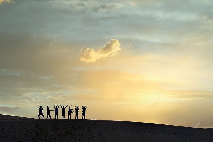 Die Silhuette von 5 Menschen vor der auf- oder untergehenden Sonne. 