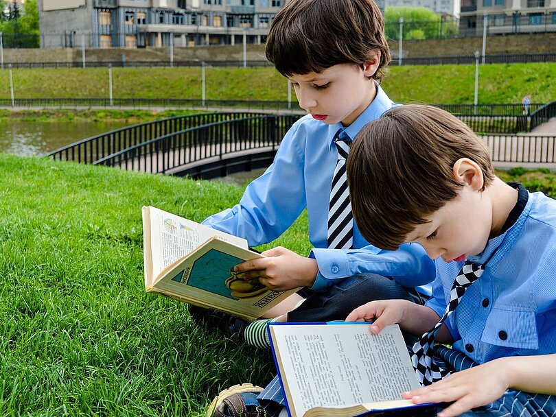 Zwei Jungs sitzen auf einer Wiese und lesen 