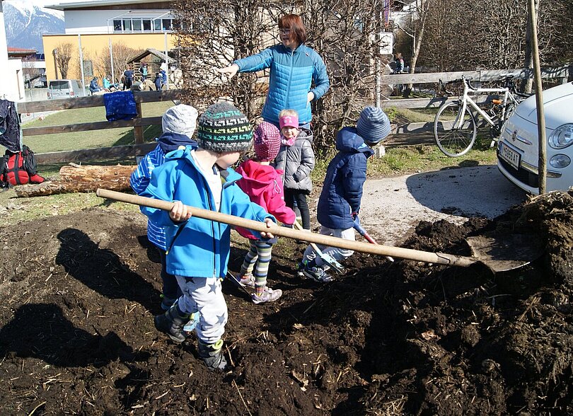 Kinder arbeiten mit Schaufeln und anderem Werkzeug auf einem Erdhaufen. 