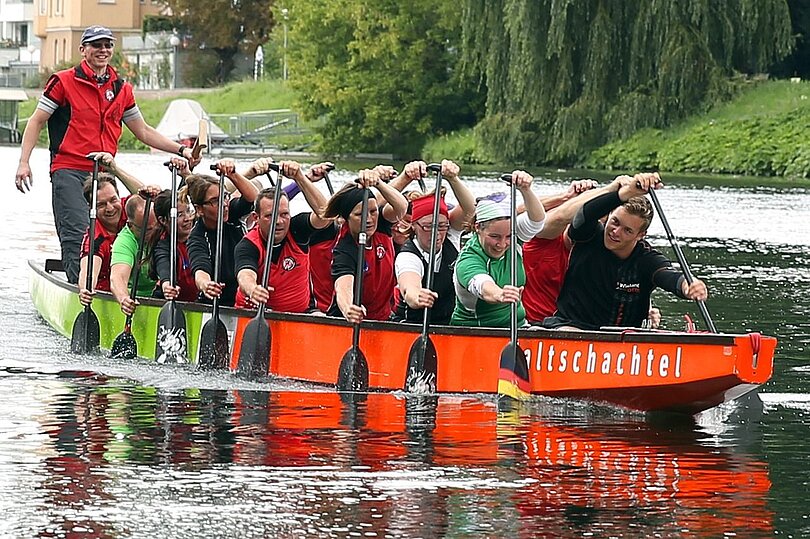 Ein Team von ca 15 Personen sitzt in einem Drachenboot beim Rudern.