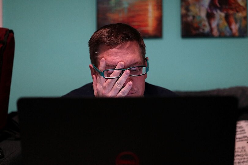 Ein Mann sitzt am PC und reibt sich müde die Augen.