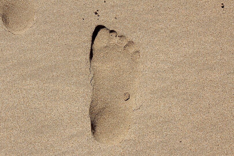 Eine einzelne Fußspur im nassen Sand.