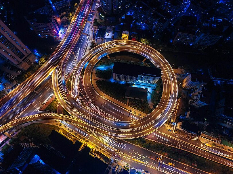 Eine Auffahrt auf eine Stadtautobahn aus der Vogelperspektive bei Nacht.  