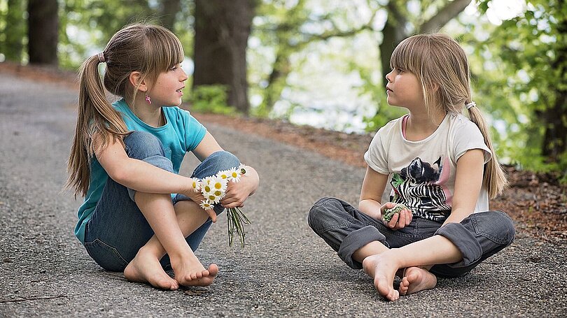 Zwei Mädchen sitzen auf einem Weg und sind in ihr Gespräch vertieft