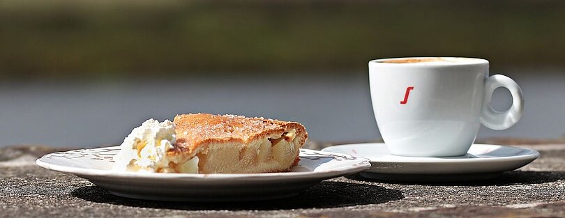 Ein Teller mit einem gedeckten Apfelkuchen und Schlagsahne und eine Tasse Kaffee 