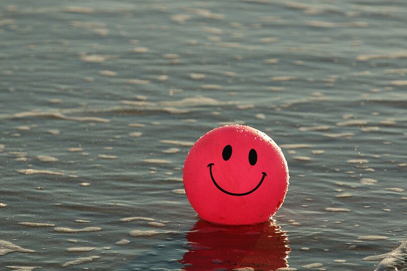 roter Luftballon mit Lachgesicht schwimmt am Wasser (See) 