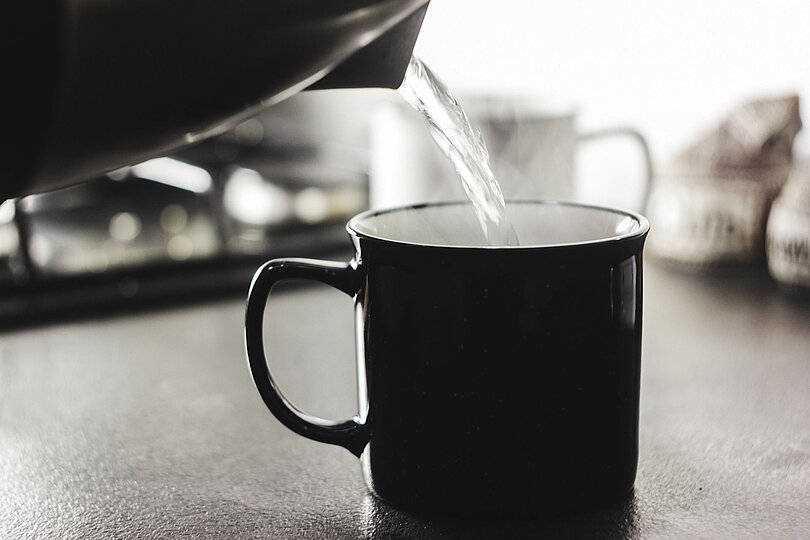 In eine schwarze Tasse wird kochendes, dampfendes Wasser eingeschenkt.