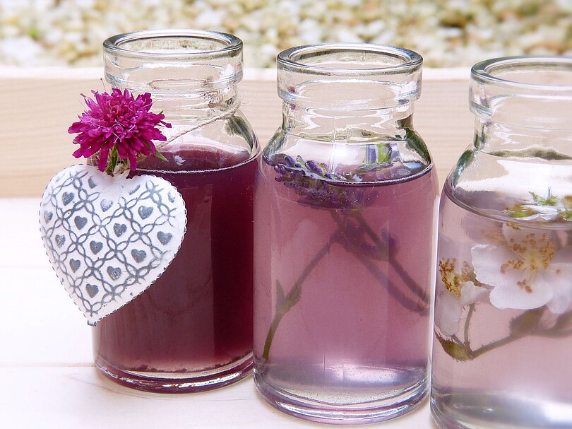Drei kleine Glasflaschen gefüllt mit eine Flüssigkeit und Rosenblättern oder Lavendelblüten oder Kleeblüten