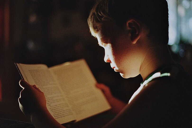 Ein Bub hält ein Buch in der Hand und liest sehr konzentriert