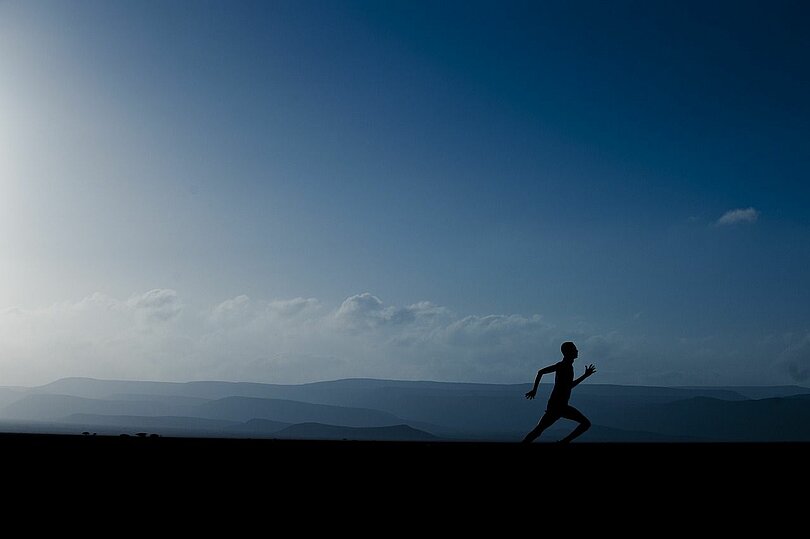 Man sieht die schwarze Silhouette eines Läufers, im Hintergrund der blaue Abendhimmel und es wirkt es gebirgig. 