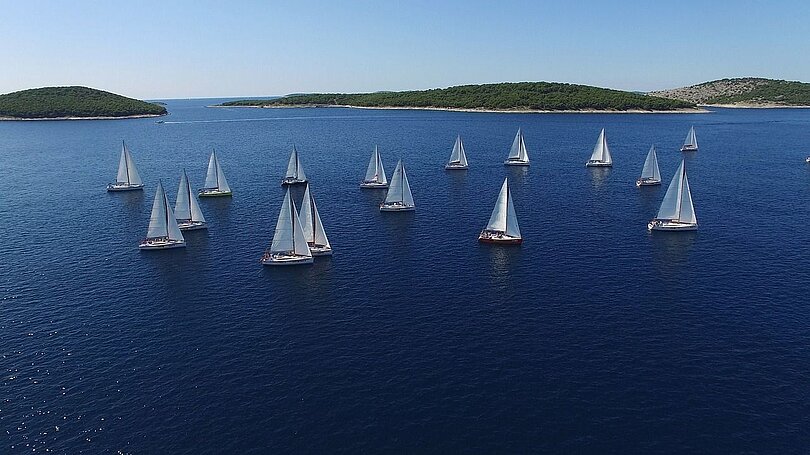 Ein Dutzend Segelschiffe mit weißen Segeln segeln am See. 