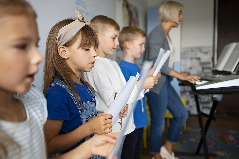 4 Kinder Kinder halten ein Notenblatt in der Hand und singen gemeinsam 
