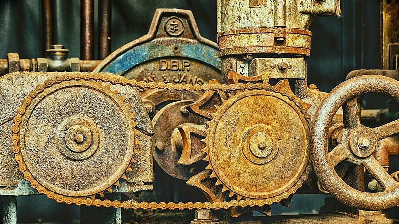 Zwei Räder einer alten Maschine sind mit einer Kette verbunden. 