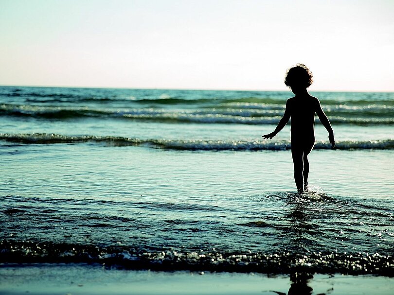 Ein Kind geht im seichten Wasser ein paar Schritte ins Meer hinein.