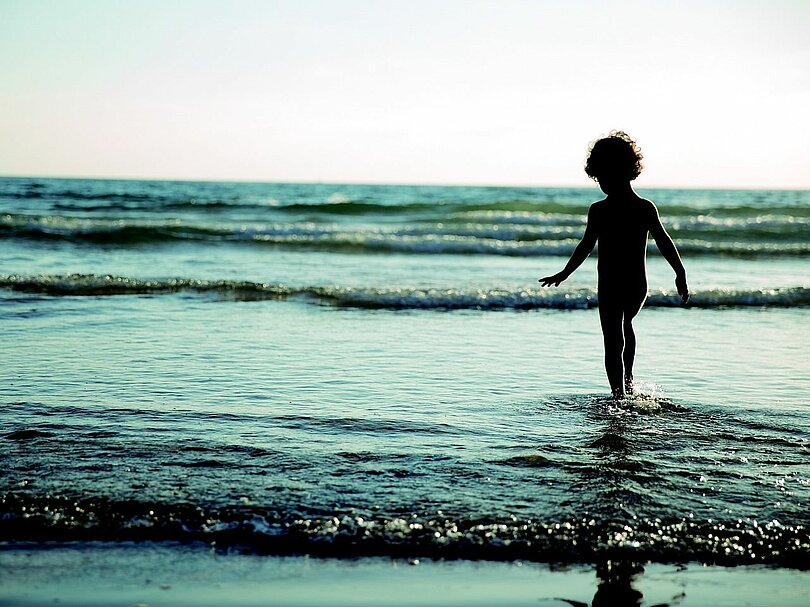 Ein Kind geht im seichten Wasser ein paar Schritte ins Meer hinein. 