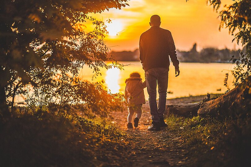 Vater und Kind spazieren bei Sonnenuntergang zu einem See