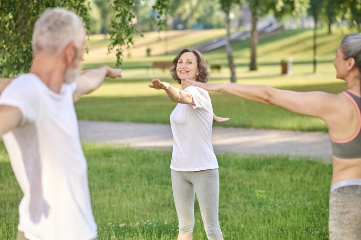 Drei Menschen stehen in Sportkleidung im Park und machen Übungen. 